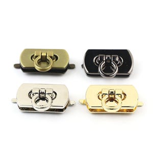 May include: Four metal purse clasps in gold, silver, black, and brass tones. Each clasp features a rectangular base with a ring pull. The clasps are designed for bags and other craft projects.