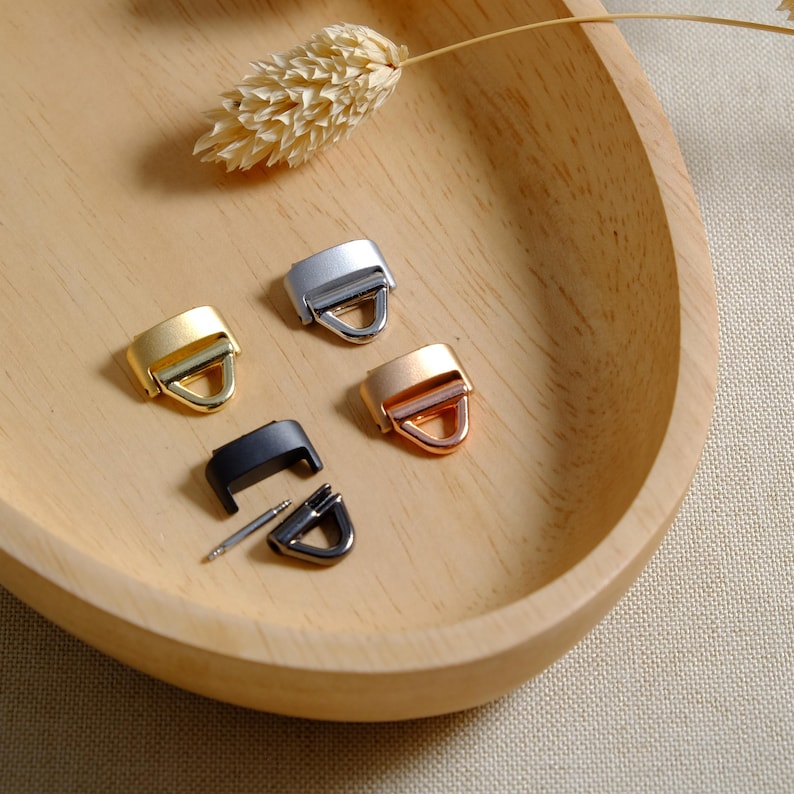 May include: Four metal clasps in different finishes: silver, gold, rose gold, and black. The clasps are displayed on a wooden surface.