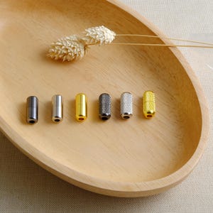 May include: Six metal cord ends in different finishes: black, silver, gold, black with a textured finish, silver with a textured finish, and gold with a textured finish.