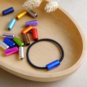 May include: A wooden bowl filled with colorful metal beads and a black elastic hair tie with a blue metal bead accent.