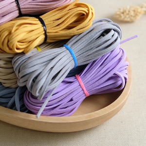 May include: A wooden bowl filled with different colors of elastic cord. The colors are purple, gray, beige, yellow, and pink.