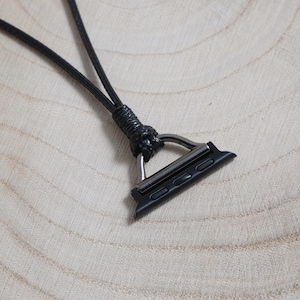May include: Black watch band adapter with a black leather cord. The adapter has a silver-coloured metal loop and is designed to connect to a smartwatch. The cord is knotted at the top.