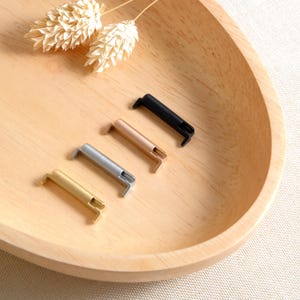 Puede incluir: Cinco adaptadores de correa de reloj en un cuenco de madera. Los adaptadores son de diferentes colores: negro, dorado, dorado rosa y plateado.
