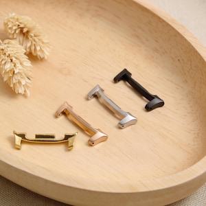 Peut inclure: Quatre adaptateurs de bracelet de montre en métal aux finitions or, or rose, argent et noir. Chaque adaptateur présente une barre horizontale avec deux petites broches verticales à chaque extrémité, conçue pour relier un bracelet à un boîtier.
