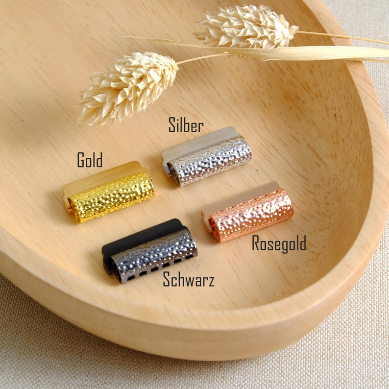 May include: Four metal slider clasps in different colors: silver, gold, rose gold, and black. Each clasp has a textured surface.