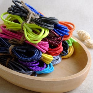 Könnte beinhalten: Eine Sammlung bunter elastischer Schnürsenkel mit weißen Punkten. Die Schnürsenkel sind gebündelt und mit Schnur zusammengebunden. Die Schnürsenkel befinden sich in einer Holzschale.