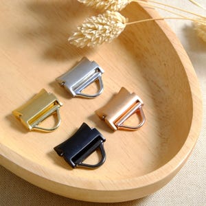 May include: Four metal slider buckles in different finishes: gold, silver, black, and rose gold. Each buckle has a D-ring.