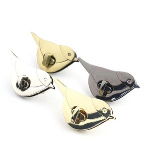 May include: Four bird-shaped metal clasps in gold, silver, and gunmetal finishes. Each clasp has a curved beak and a circular eye detail. The clasps are designed for use in bags or other craft projects.