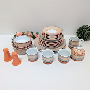 Könnte beinhalten: Ein komplettes Geschirrset mit Tellern, Schalen, Tassen, einem Sahnekännchen und einer Zuckerdose. Das Set hat einen beigefarbenen Hintergrund mit einem geometrischen Muster in Orange, Blau und Grün. Zwei orangefarbene Salz- und Pfefferstreuer sind ebenfalls enthalten.