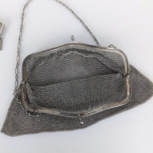 May include: A silver mesh purse with a chain strap. The purse is open and the inside is visible. The purse is made of a fine mesh material.