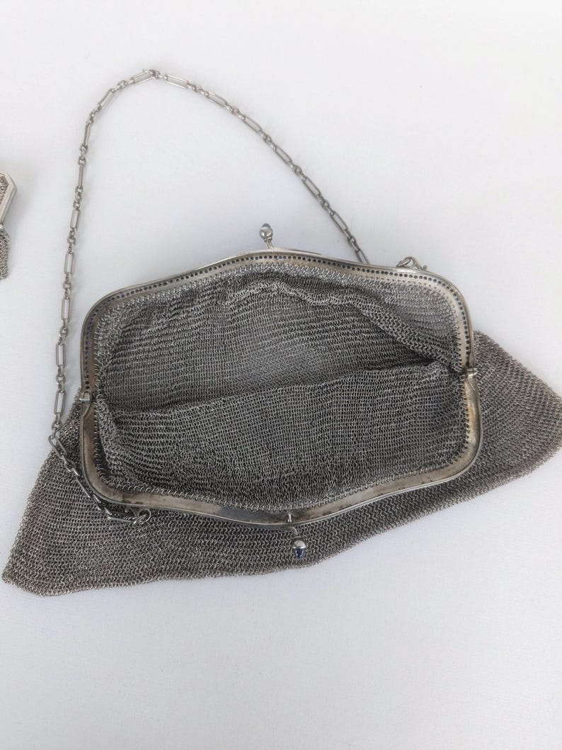 May include: A silver mesh purse with a chain strap. The purse is open and the inside is visible. The purse is made of a fine mesh material.