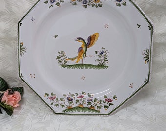 Pode incluir: Prato de cerâmica octogonal com um desenho de pássaro verde, amarelo e roxo. O pássaro é rodeado por folhas verdes e flores rosa, amarelas e azuis. O prato tem um fundo branco e uma borda verde.