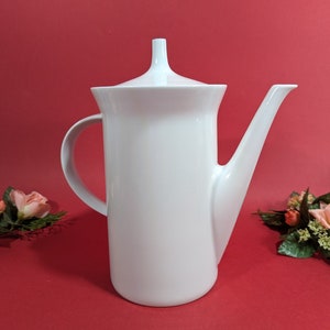 May include: A white ceramic coffee pot with a lid and a spout. The pot has a simple, modern design.