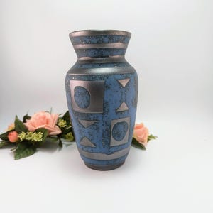 May include: A blue ceramic vase with silver geometric shapes and horizontal bands. The vase has a textured surface and a flared top. Decorative vase for home decor.