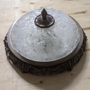 May include: A round, frosted glass ceiling light fixture with a decorative bronze frame and a bronze finial.