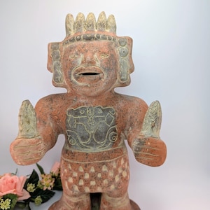 Könnte beinhalten: Terrakottafarbene Figur einer stehenden Figur mit erhobenen Armen. Die Figur hat ein detailliertes Gesicht, einen Kopfschmuck und ein gemustertes Design am Unterkörper. Die Statue ist wahrscheinlich ein Dekorationsartikel.