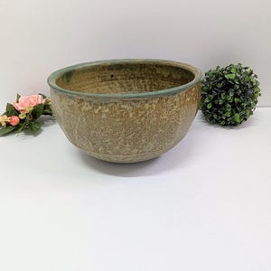 Może przedstawiać: Okrągła ceramiczna miska o teksturowanym, nakrapianym wykończeniu zewnętrznym w odcieniach beżu i brązu. Krawędź miski posiada wyraźną, gładką, turkusowo-zieloną glazurę, która kontrastuje z ziemistymi, nakrapianymi odcieniami korpusu naczynia.