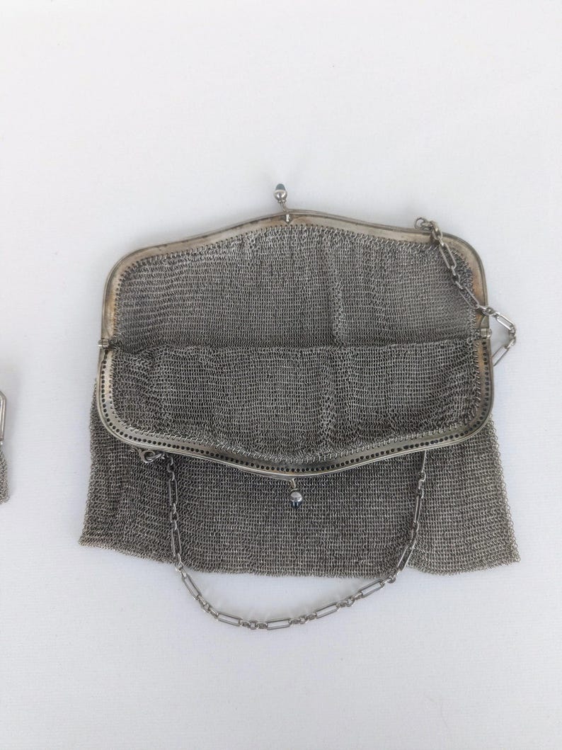 May include: A silver mesh evening bag with a chain strap. The bag is open and the interior is visible.