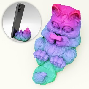 May include: A rainbow coloured cat phone stand with a phone in the stand. The cat is holding a small pink rectangle in its paws.