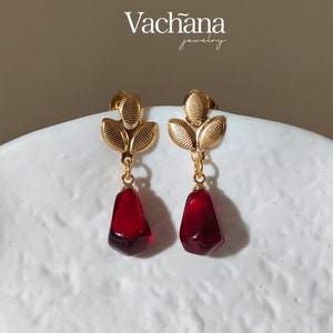 May include: Gold earrings with a three-leaf design and a dangling red teardrop-shaped stone.