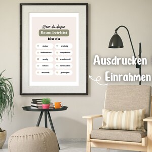 May include: A printable wall art poster with a light pink background and green and white text. The text reads "Wenn du diesen Raum betrittst bist du" and lists a series of positive adjectives in German. The poster is framed and hanging on a wall in a living room setting.