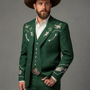 May include: A green three-piece suit with floral embroidery and white accents. The suit includes a jacket, vest, and pants. The person is wearing a brown cowboy hat and a belt with a decorative buckle. The suit is a classic Western style.