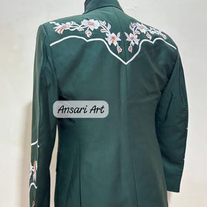 May include: A dark green blazer with white and orange floral embroidery on the back and sleeve. The blazer has a classic design with a notched lapel and buttoned cuffs. The text "Ansari Art" is visible on the front.
