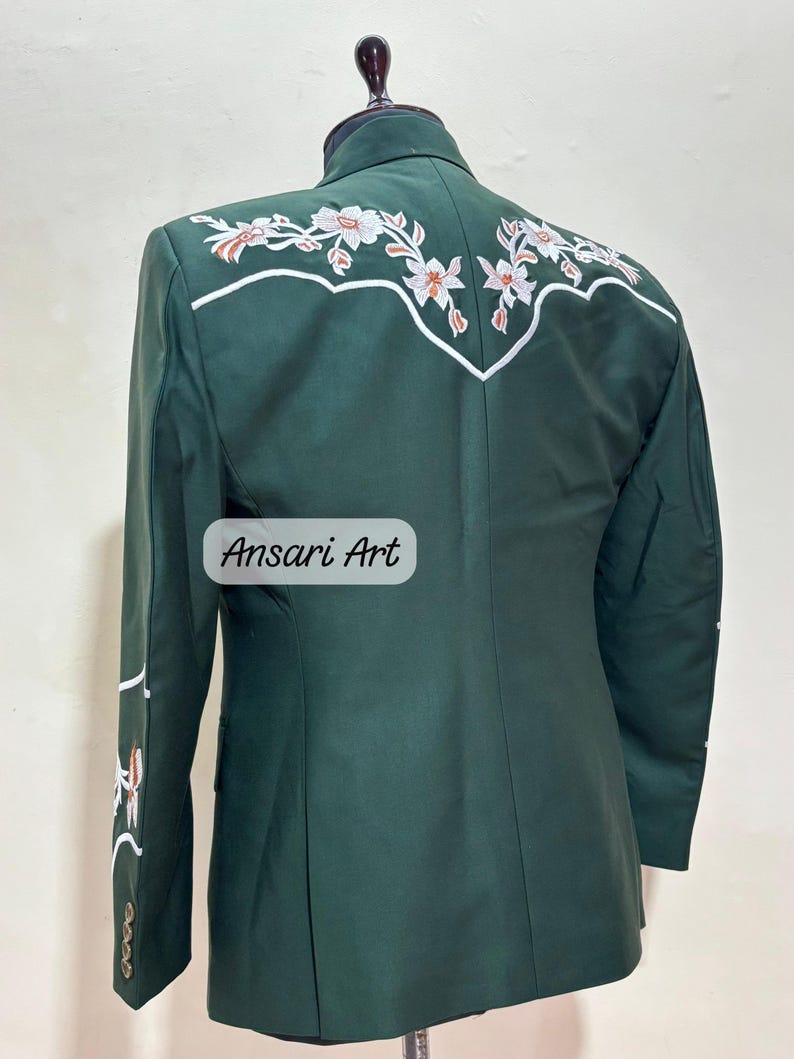 May include: A dark green blazer with white and orange floral embroidery on the back and sleeve. The blazer has a classic design with a notched lapel and buttoned cuffs. The text "Ansari Art" is visible on the front.