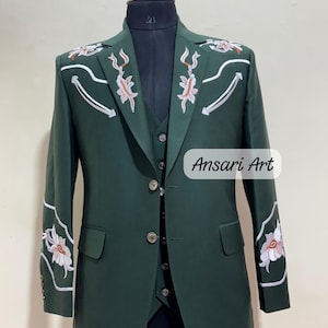 May include: A dark green suit with floral embroidery on the shoulders and sleeves. The suit includes a blazer, vest, and pants, displayed on a mannequin. The text "Ansari Art" is visible on the lower right.