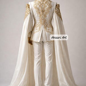 May include: A white formal suit with gold embroidery, featuring a long cape and matching headwear. The suit has intricate gold detailing on the shoulders and back. Gold shoes complete the ensemble. The text "Ansari Art" is visible.