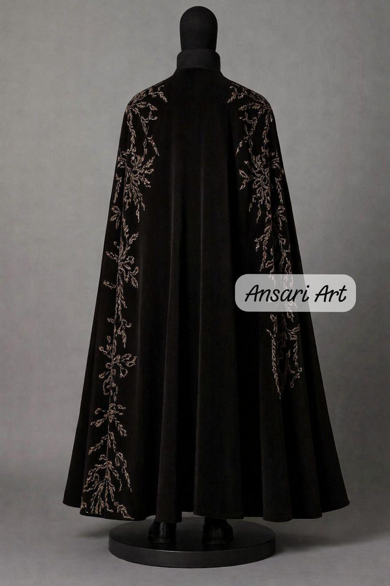 May include: Black velvet cloak with intricate floral embroidery in a contrasting color. The cloak features a high collar and a flowing design, with the text "Ansari Art" on the lower right side.