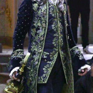 Puede incluir: Una chaqueta azul y verde bordada con botones dorados y un cuello de encaje blanco.