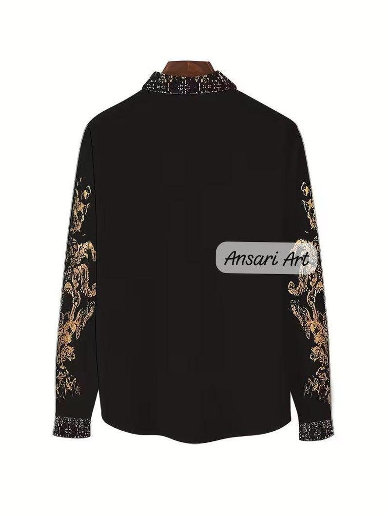 May include: Black button-down shirt with gold floral patterns on the sleeves and collar. The shirt has the text "Ansari Art" on the lower right side. The collar and cuffs have a patterned design.