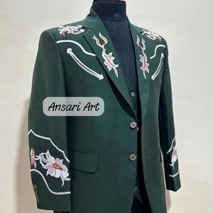 May include: A dark green suit with floral embroidery. The suit includes a blazer and vest, displayed on a mannequin. White and orange floral designs with white accents adorn the shoulders and sleeves. The text "Ansari Art" is visible.