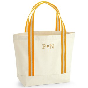 May include: A white canvas tote bag with orange and white striped handles. The bag has the initials "P &hearts; N" embroidered on the front.