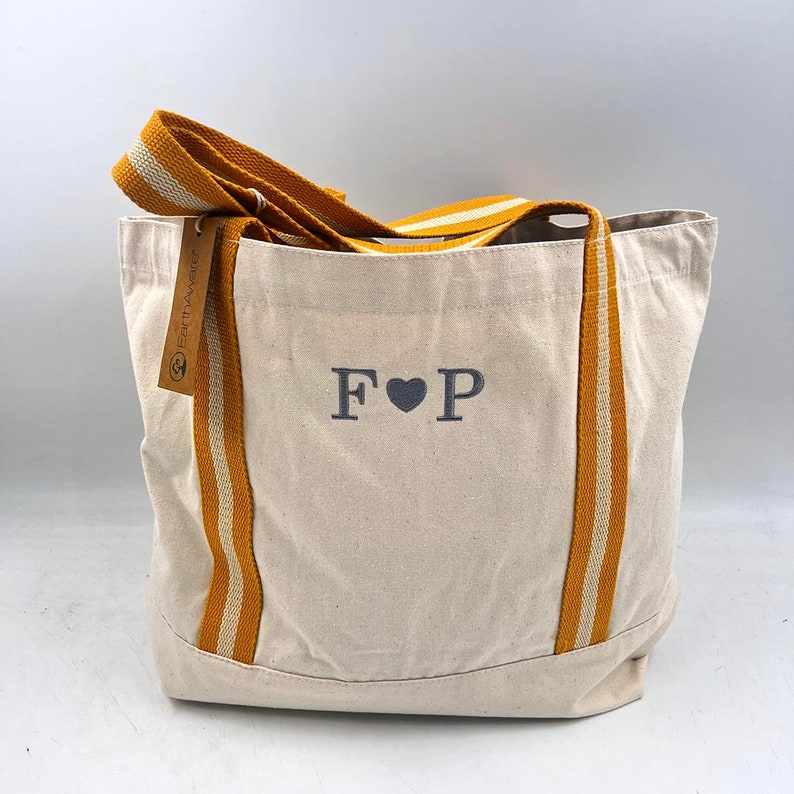 May include: A white canvas tote bag with yellow and white striped straps. The bag has the letters "F &hearts; P" embroidered on the front.