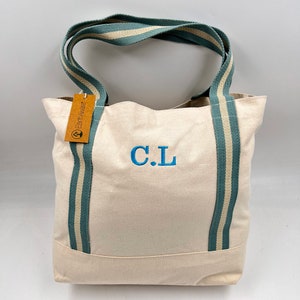May include: A white canvas tote bag with teal and white striped straps. The bag has a brown tag that says "Earthwise" and the initials "C.L." are embroidered on the front in blue.