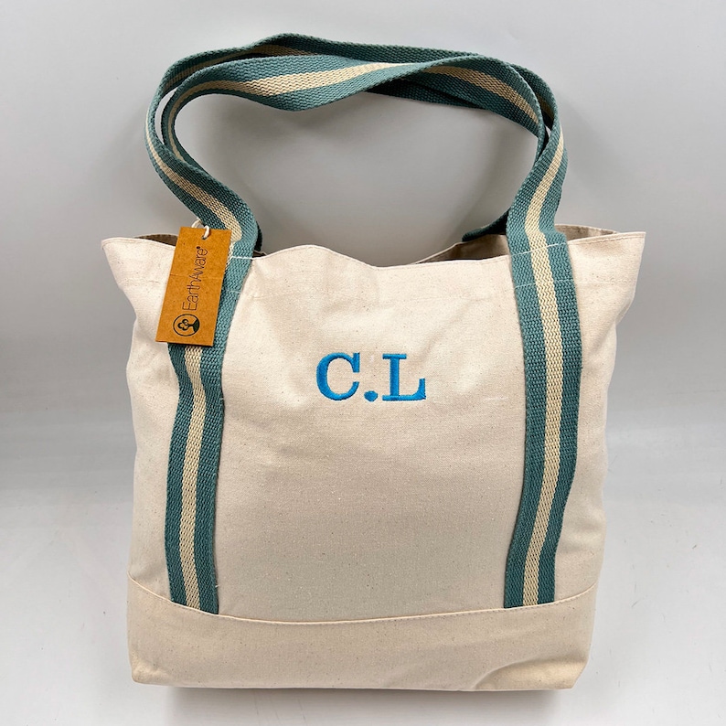 May include: A white canvas tote bag with teal and white striped straps. The bag has a brown tag that says "Earthwise" and the initials "C.L." are embroidered on the front in blue.