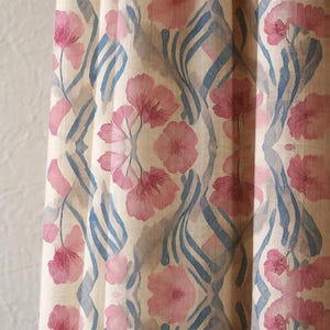 Könnte beinhalten: Nahaufnahme eines Stoffes mit einem sich wiederholenden Blumenmuster. Rosa Blüten und blaue, geschwungene Linien vor cremefarbenem Hintergrund. Der Stoff hat ein strukturiertes Aussehen, das auf Leinen oder ein ähnliches Material hindeutet.