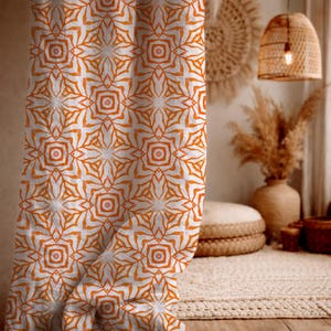 May include: A curtain with a repeating geometric pattern in orange and white. The design features stylized floral or star-like shapes. The curtain is draped, with folds visible, suggesting a soft fabric. The overall aesthetic is bohemian or coastal, with a warm colour palette.