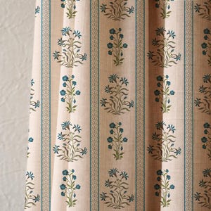 K&ouml;nnte beinhalten: Cremefarbener Stoff mit einem sich wiederholenden Blumenmuster in T&uuml;rkis und Blau. Vertikale t&uuml;rkisfarbene Streifen mit einem blattartigen Design umranden die floralen Motive. Der Stoff hat ein strukturiertes Aussehen, was auf Leinen oder ein &auml;hnliches Material hindeutet.