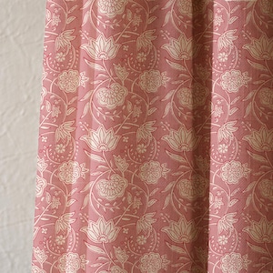 May include: Close-up of a pink floral patterned fabric. The fabric features a repeating design of white flowers and leaves on a pink background. The fabric is likely used for curtains or upholstery.