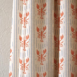 May include: Cream-coloured fabric featuring a repeating pattern of orange lobsters and blue vertical stripes. The fabric has a linen-like texture, suitable for curtains or upholstery.