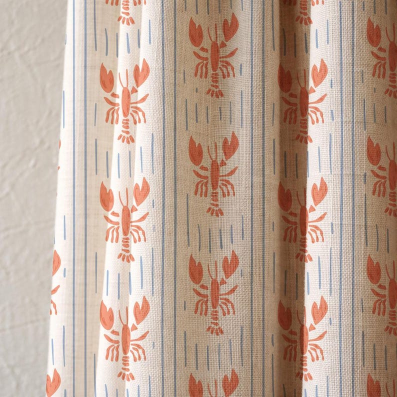 May include: Cream-coloured fabric featuring a repeating pattern of orange lobsters and blue vertical stripes. The fabric has a linen-like texture, suitable for curtains or upholstery.