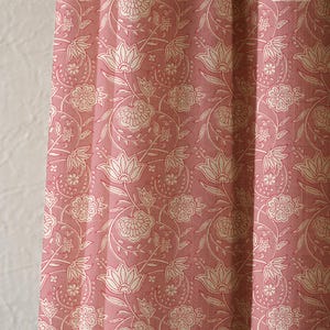 May include: Close-up of a pink floral patterned fabric. The fabric features a repeating design of white flowers and leaves on a pink background. The fabric is likely used for curtains or upholstery.