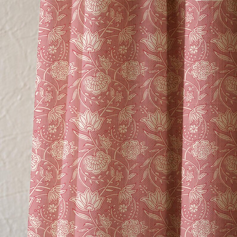 May include: Close-up of a pink floral patterned fabric. The fabric features a repeating design of white flowers and leaves on a pink background. The fabric is likely used for curtains or upholstery.