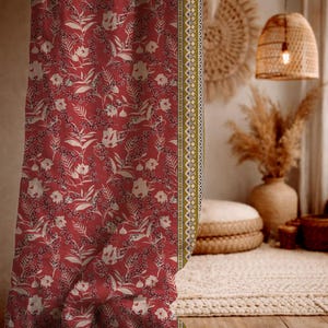 May include: Red floral patterned fabric with white flowers and leaves. A decorative border with a cream, olive green, and blue design runs along the edge. The fabric is likely used for curtains or upholstery.