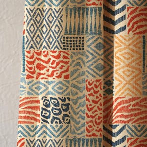Könnte beinhalten: Textil mit einem Patchwork-Design mit geometrischen und abstrakten Mustern in Blau-, Orange- und Cremetönen. Die Muster umfassen Diamanten, Zickzackmuster und tierfellartige Motive. Der Stoff hat ein strukturiertes Aussehen.