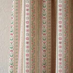 May include: Close-up of a fabric with a repeating vertical pattern. The design features alternating stripes of floral and geometric motifs in shades of pink, green, and beige. The fabric has a vintage, classic aesthetic.