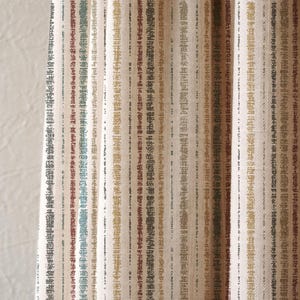 May include: Close-up of a textured fabric with vertical stripes in various neutral colours, including beige, brown, and olive green. The fabric appears to be woven, with a subtle pattern within each stripe. The overall aesthetic is natural and earthy.